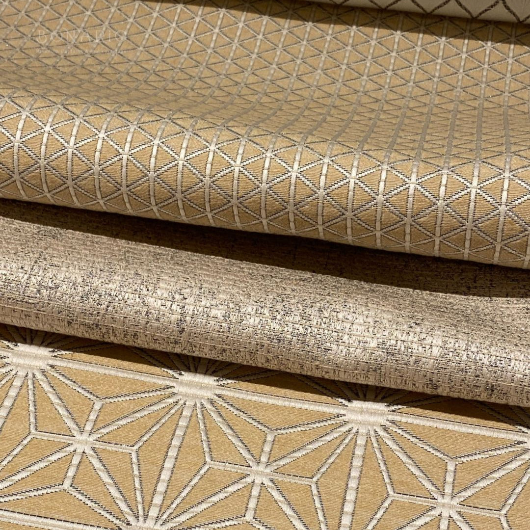 Four rolls of textured fabric with geometric patterns on a wooden surface.